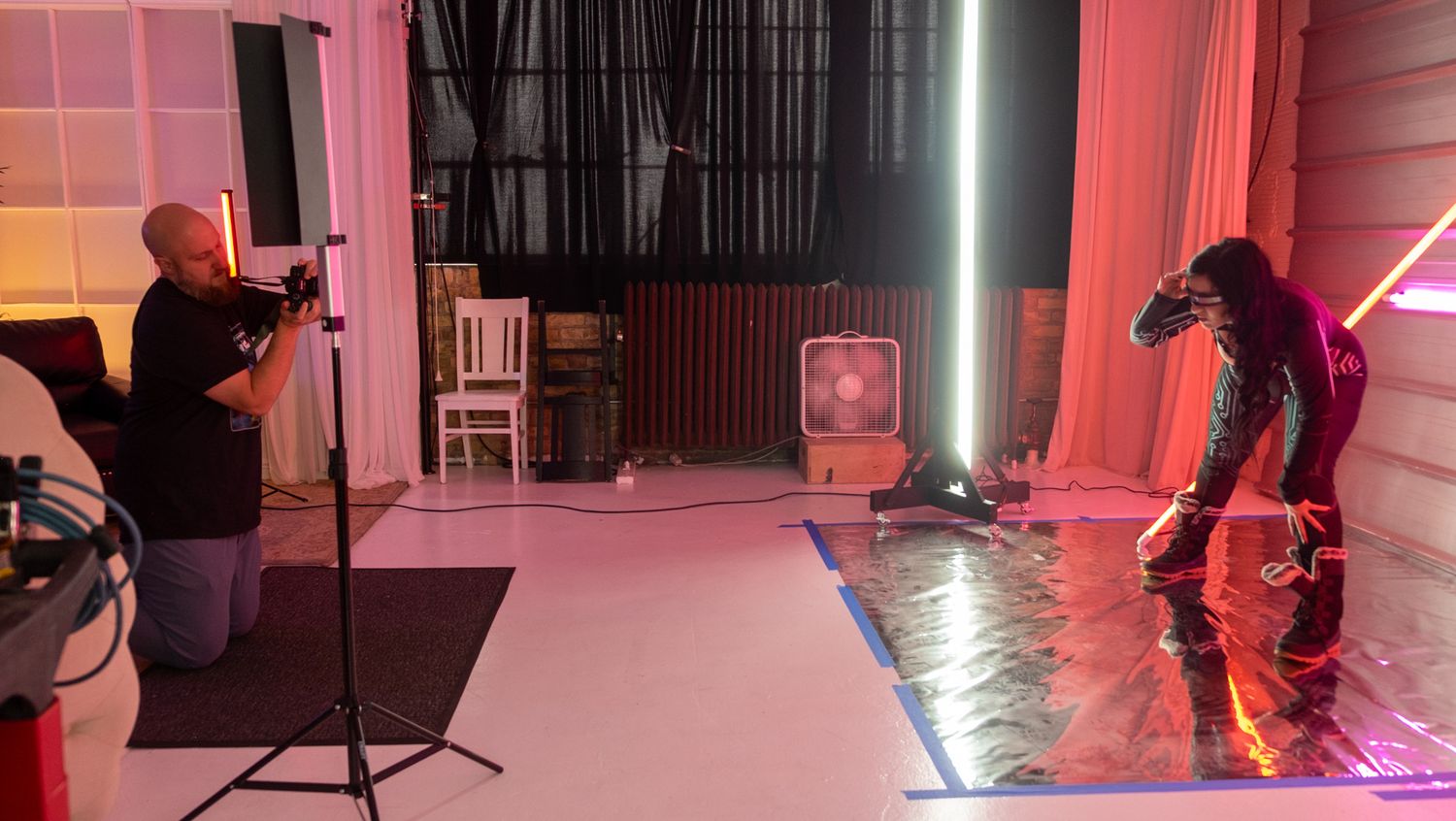 A pink-lit studio space with multiple dancers performing dynamic movements in silhouette.