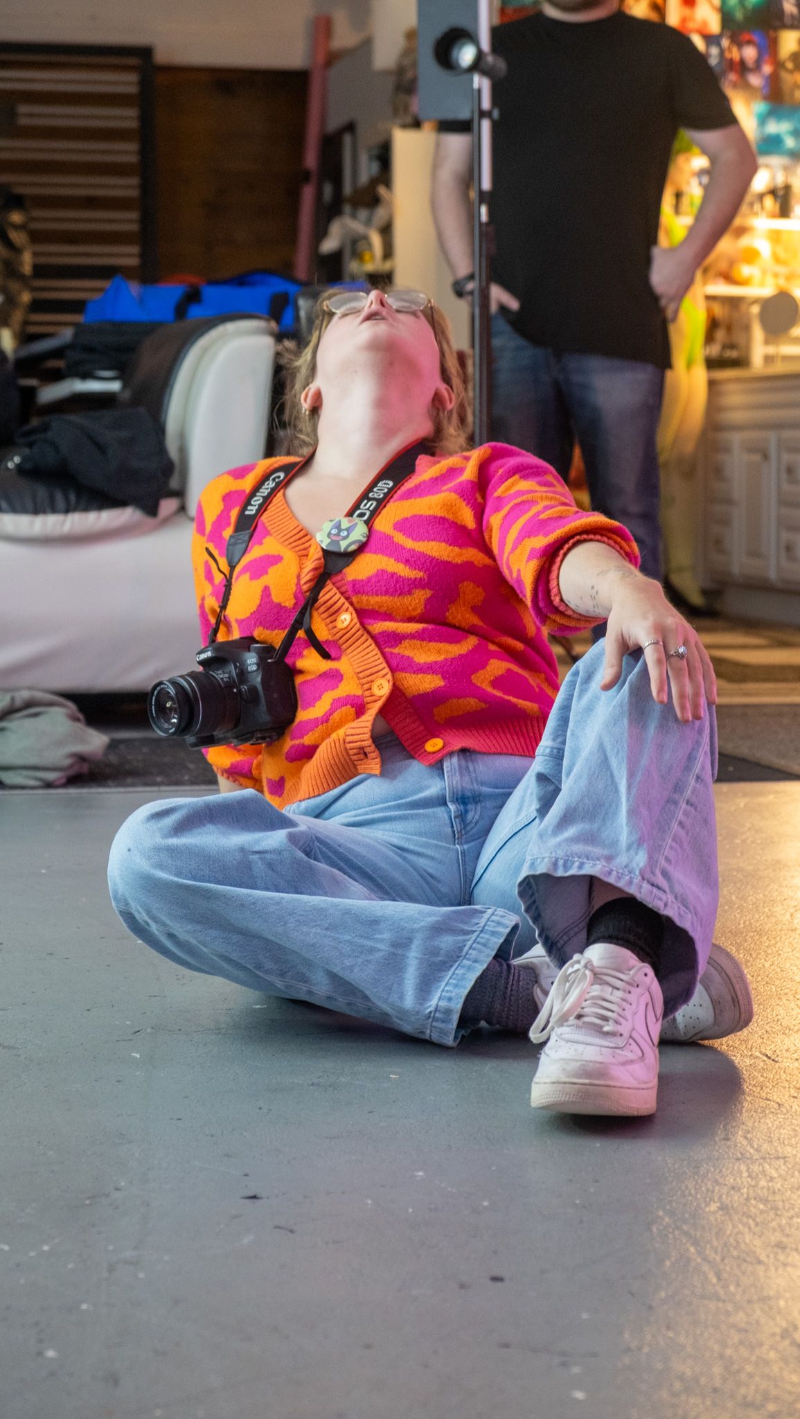 Person wearing bright orange shirt and jeans sitting on ground in urban setting with dramatic lighting.