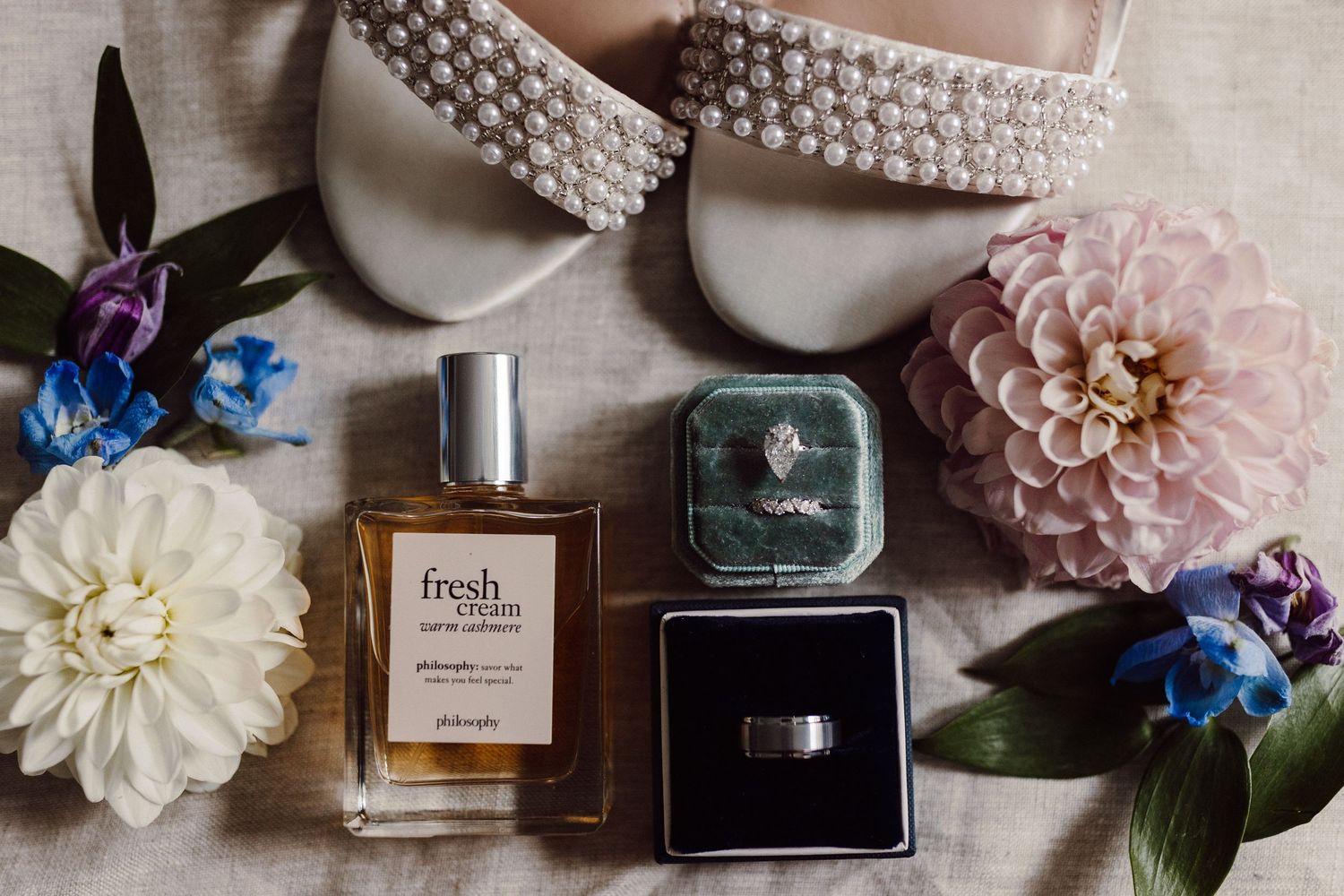 Wedding day details including perfume bottles, pearl jewelry, and delicate floral arrangements on a neutral surface.