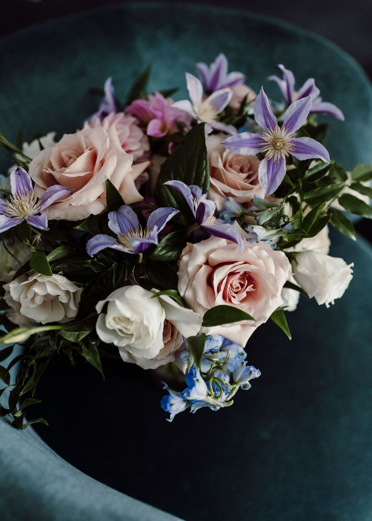 Elegant floral arrangement with purple clematis, pink roses, and blue flowers against a dark background.