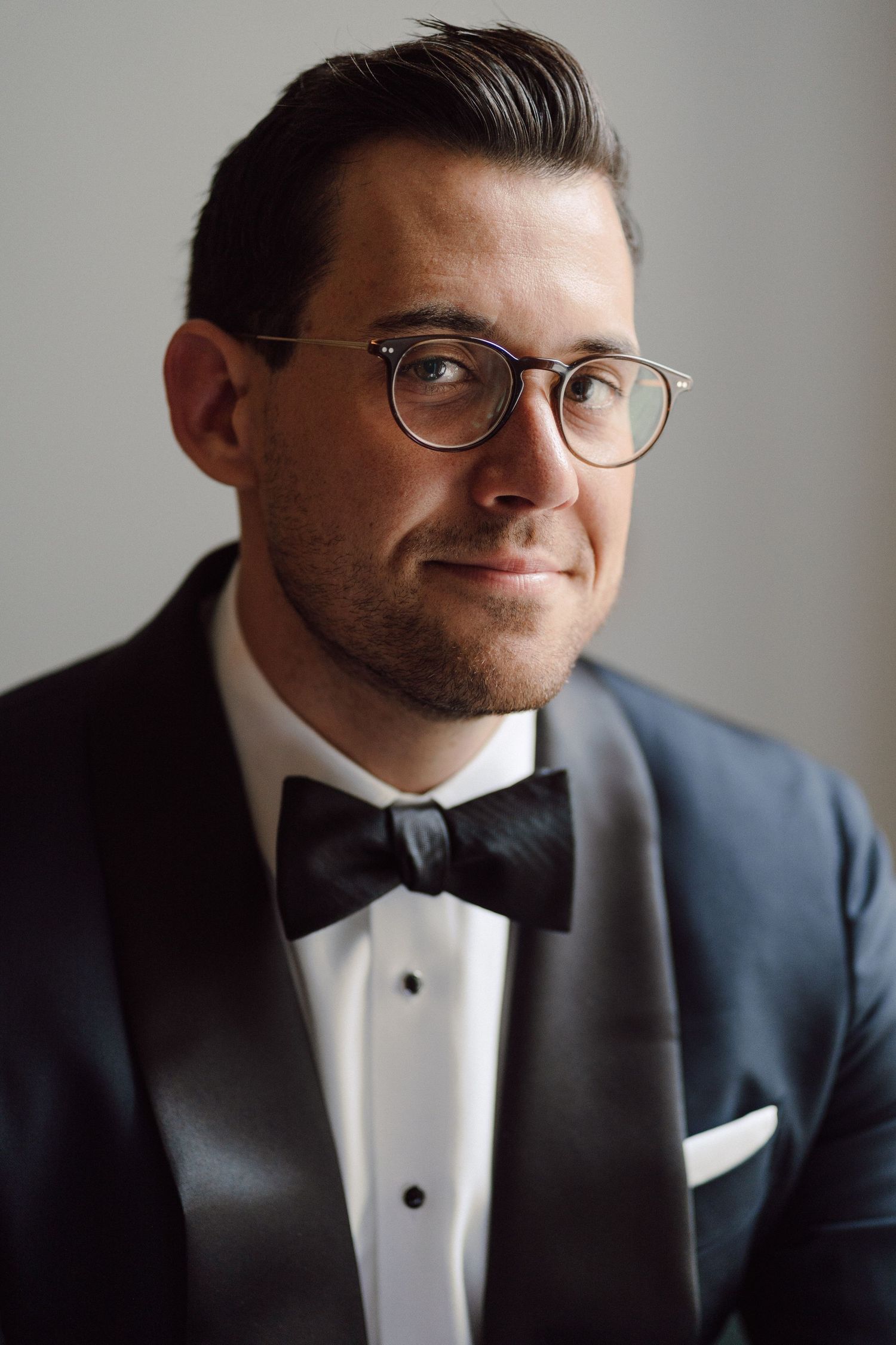 Close-up portraits of groom in tuxedo and glasses with dramatic side lighting.