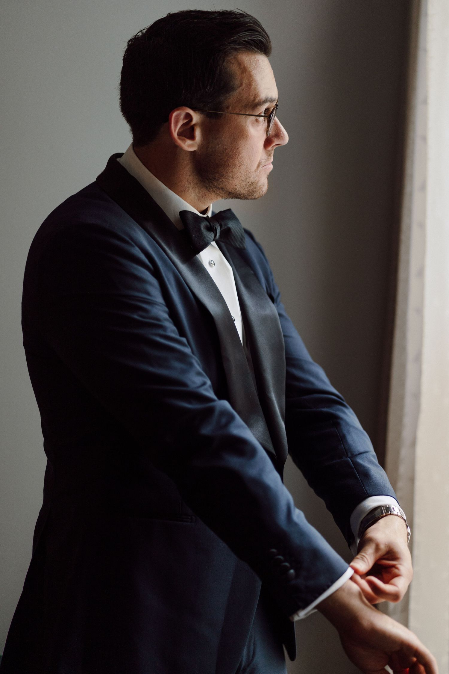 Dramatic side profile shots of a groom in a navy suit adjusting his cuffs.