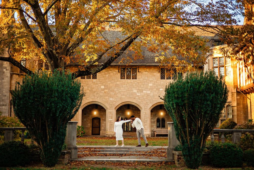 Elegant stone archway entrance with two tall topiaries and golden autumn leaves overhead at sunset.
