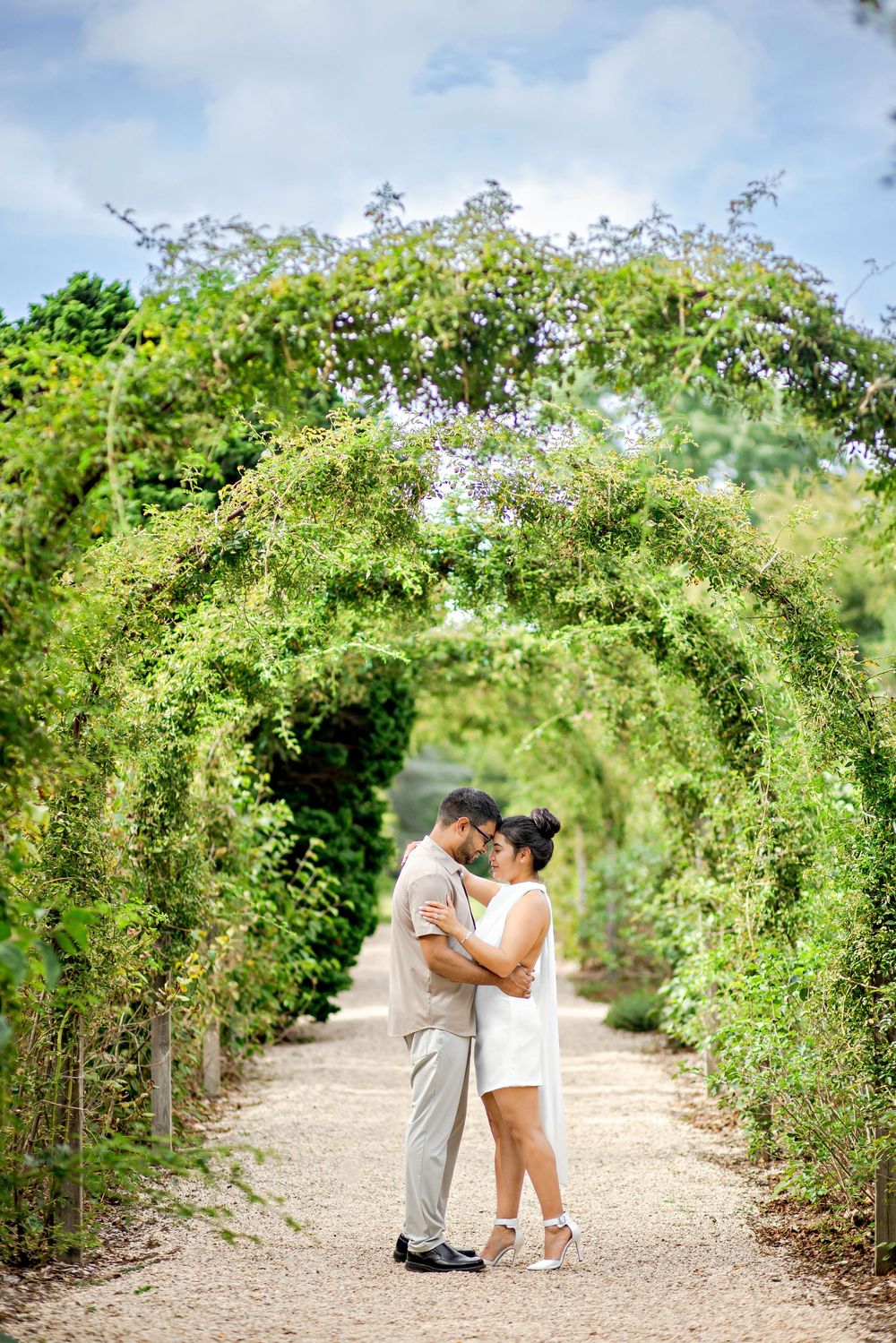 A romantic sequence captured in a garden pathway lined with lush green arches and flowering vines.