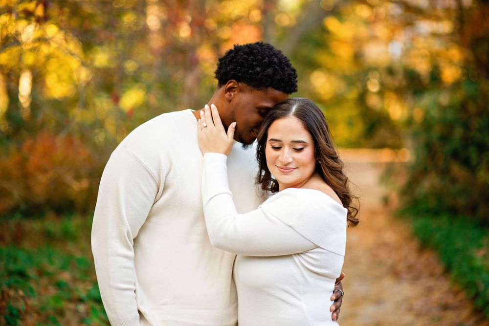 A couple in white outfits shares romantic moments during a golden sunset photoshoot in an autumn setting.