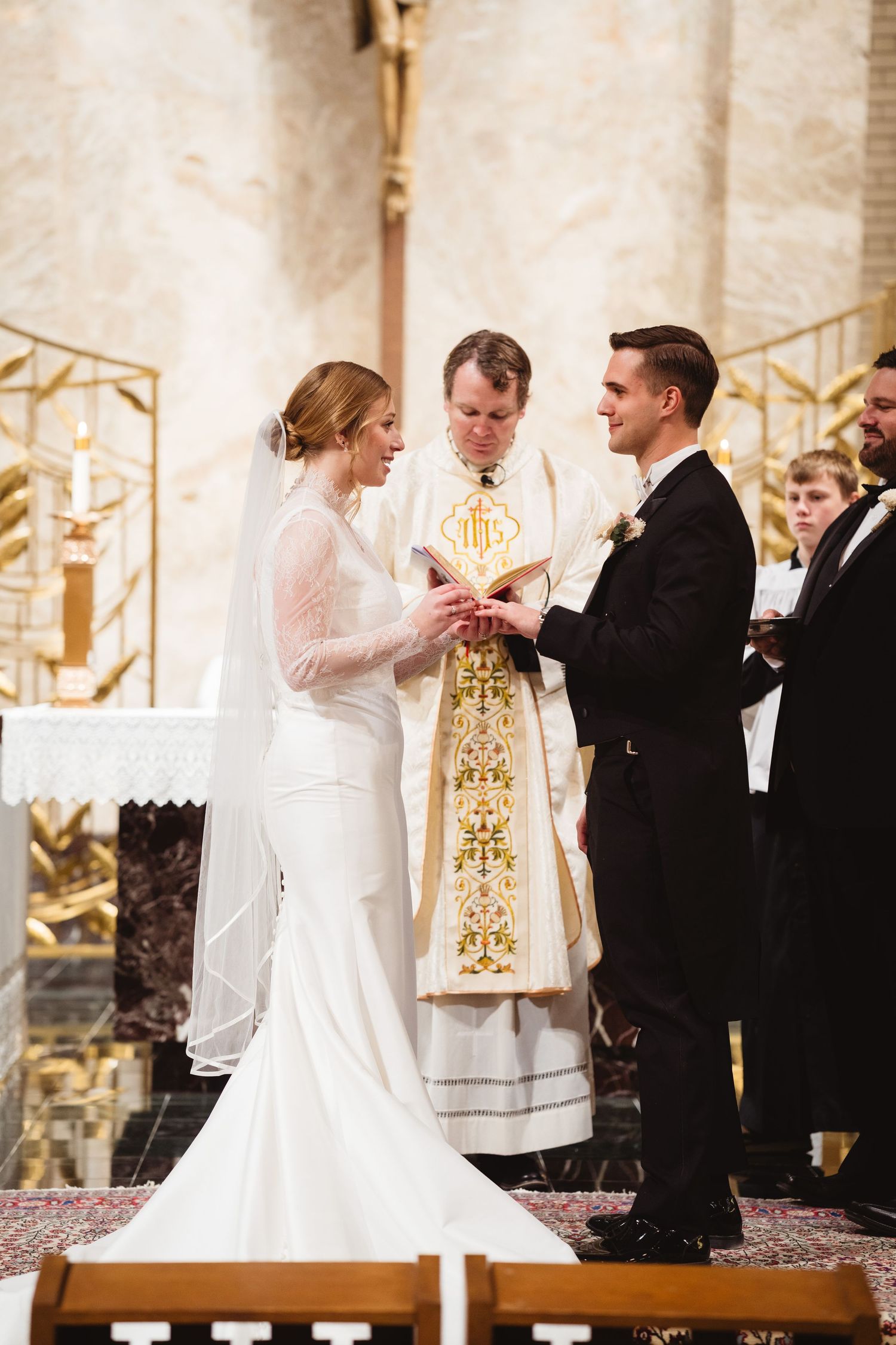 A traditional Catholic wedding ceremony shows the exchange of rings at the altar in a church setting.