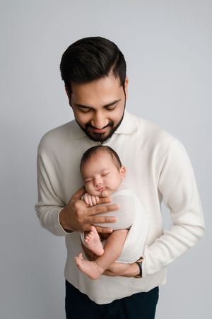 A series of tender moments showing a person in a white sweater cradling and bonding with a sleeping newborn baby.