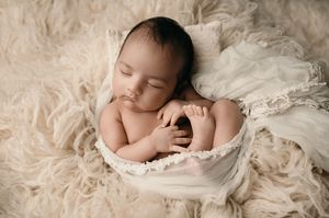 A sleeping newborn baby nestled in soft white fabric during a professional photography session.