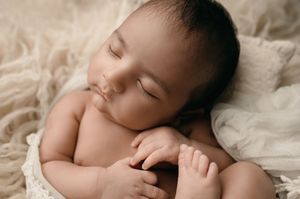 Peaceful sleeping baby curled up on soft cream-colored fabric in gentle natural lighting.