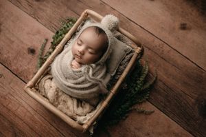 A series of baby portraits in wooden frames arranged on rustic wooden floorboards with green foliage accents.