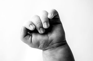 Black and white photograph of a baby's tiny hand reaching upward against a white background.