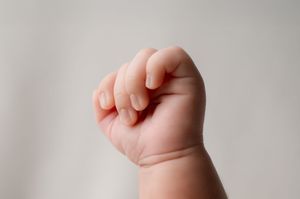 Close-up of a baby's tiny clenched fist against a light gray background.