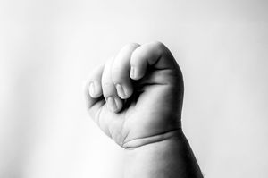 Black and white artistic photograph of an infant's small fist against a plain background.