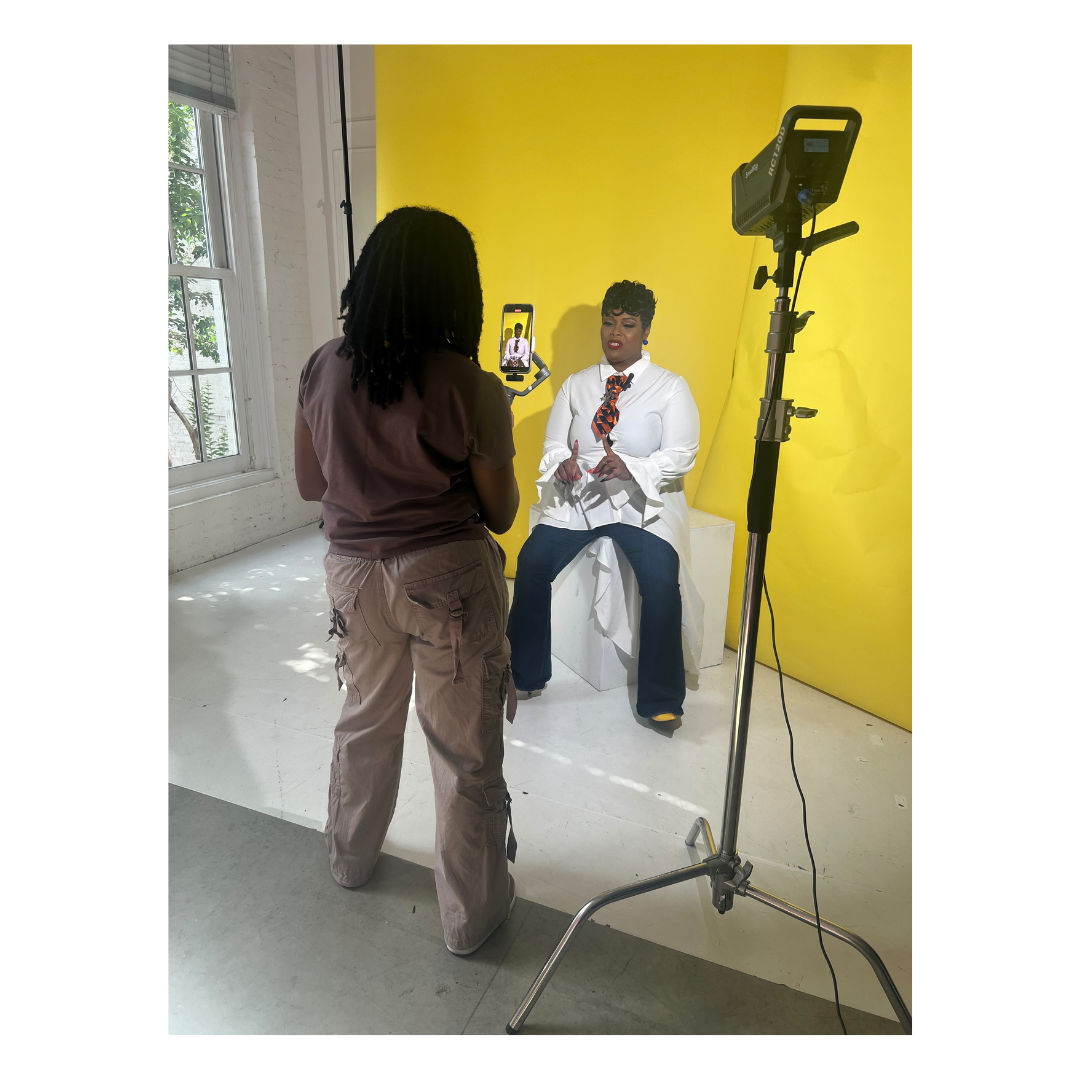 Professional photo studio setup with lighting equipment against a bright yellow wall and white floor.