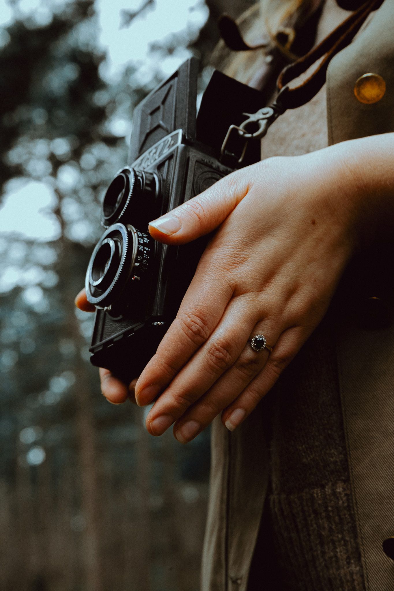 Close-up shot of hands holding a vintage camera with a black ring against in a forest.
