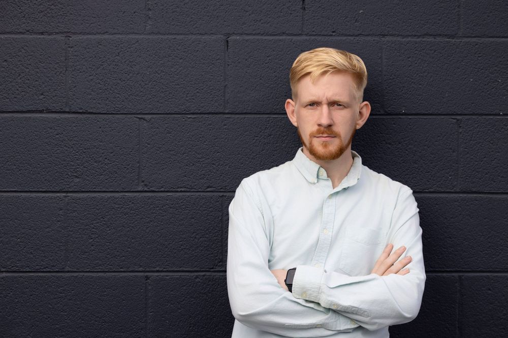 Professional headshot against dark background showing person wearing white button-up shirt.