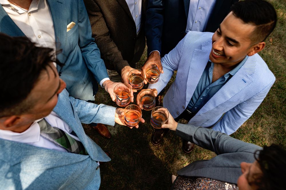 People in light blue suits clink glasses together in a celebratory toast at an outdoor gathering.