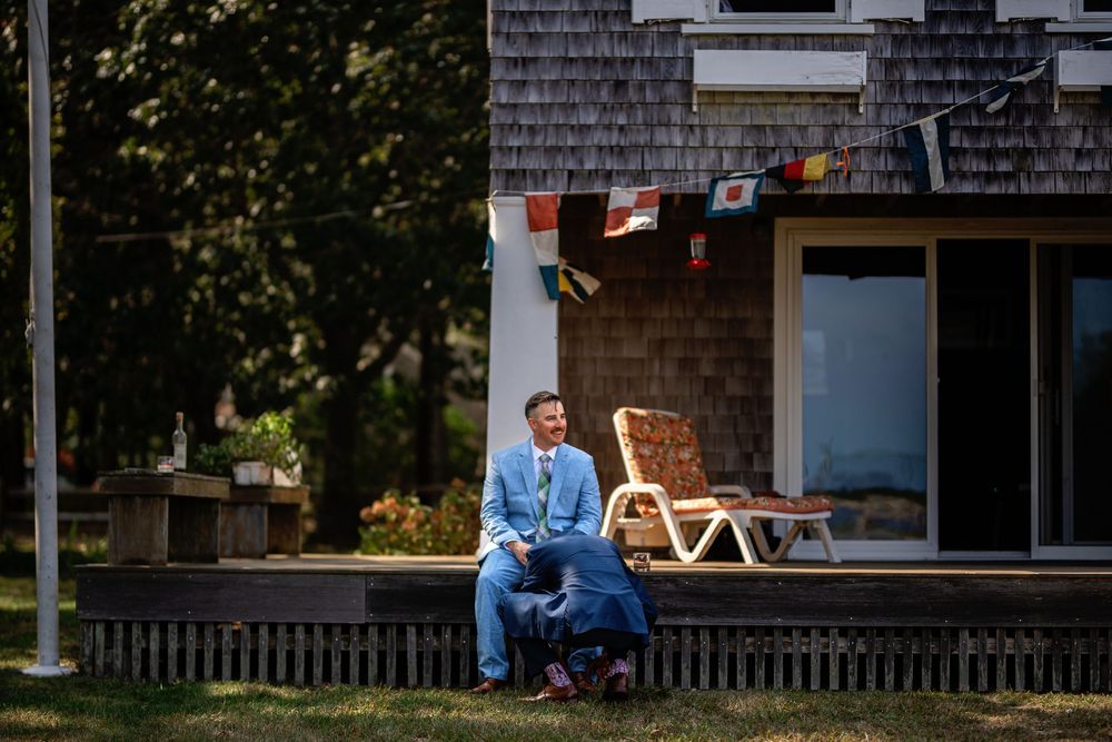 Person sits on wooden steps of a rustic cabin porch surrounded by trees and natural scenery.