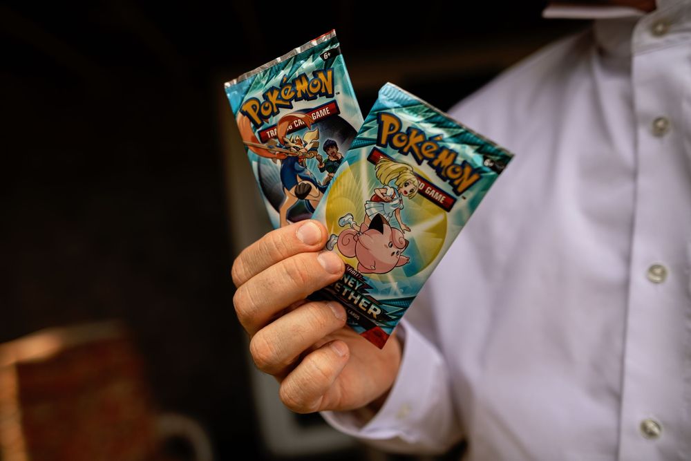 Hands holding and displaying multiple Pokemon trading card game booster packs against a dark background.
