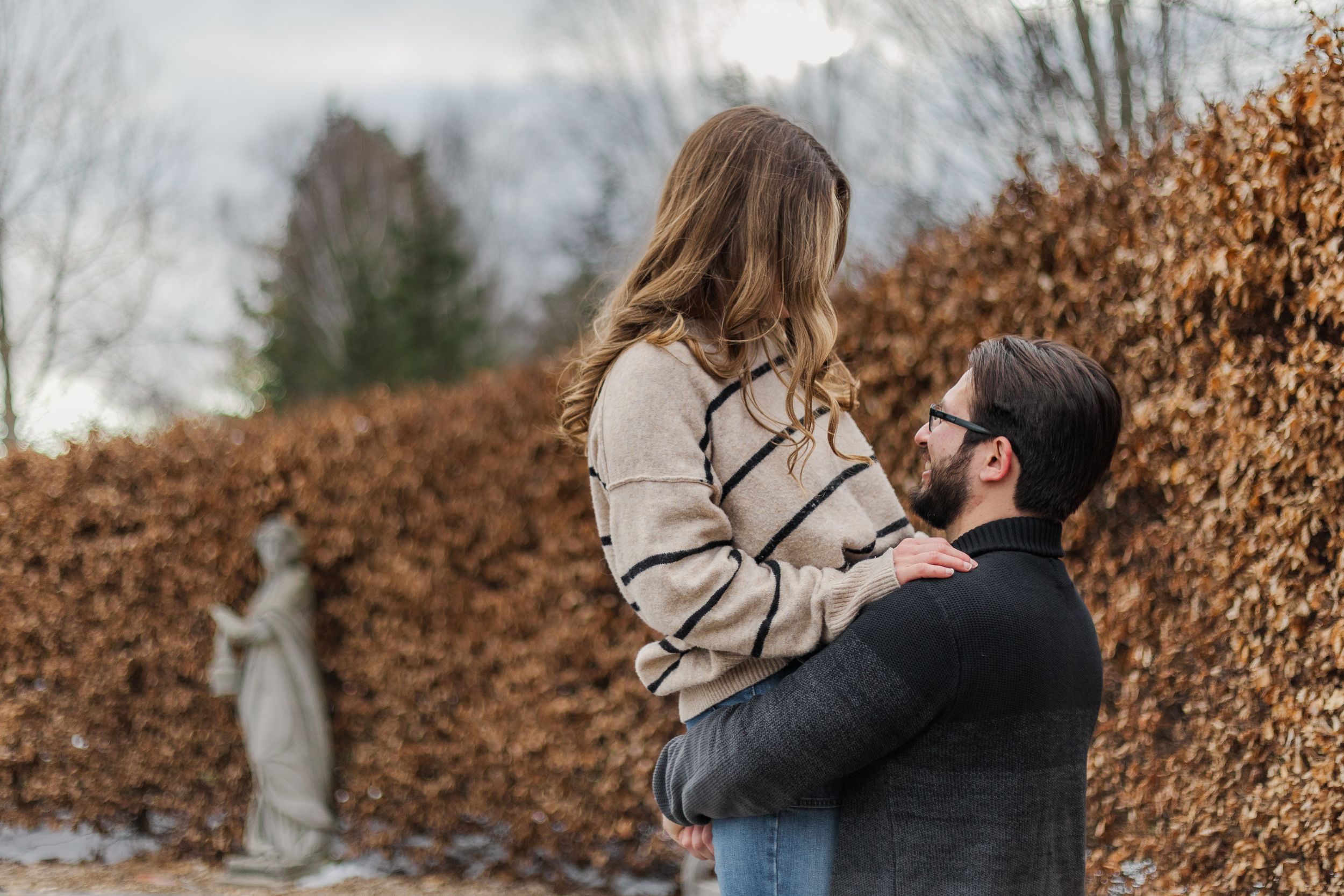 A couple shares a romantic moment outdoors surrounded by autumn foliage and muted winter colors.