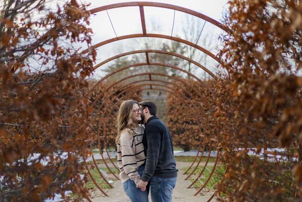 A couple embraces under an arched walkway surrounded by autumn foliage during a romantic photoshoot.