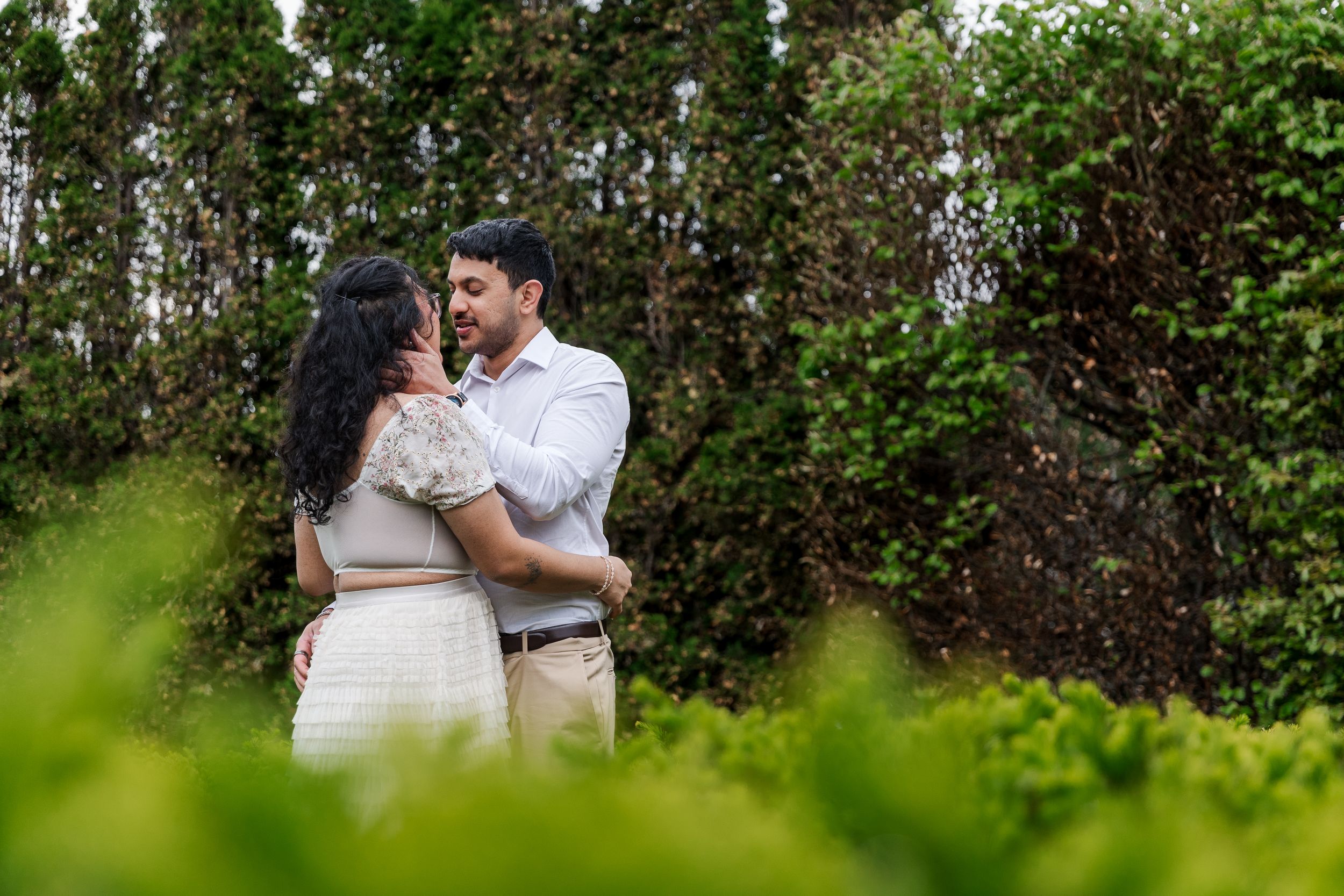 A couple shares an intimate moment in a lush garden setting during their outdoor wedding photoshoot.
