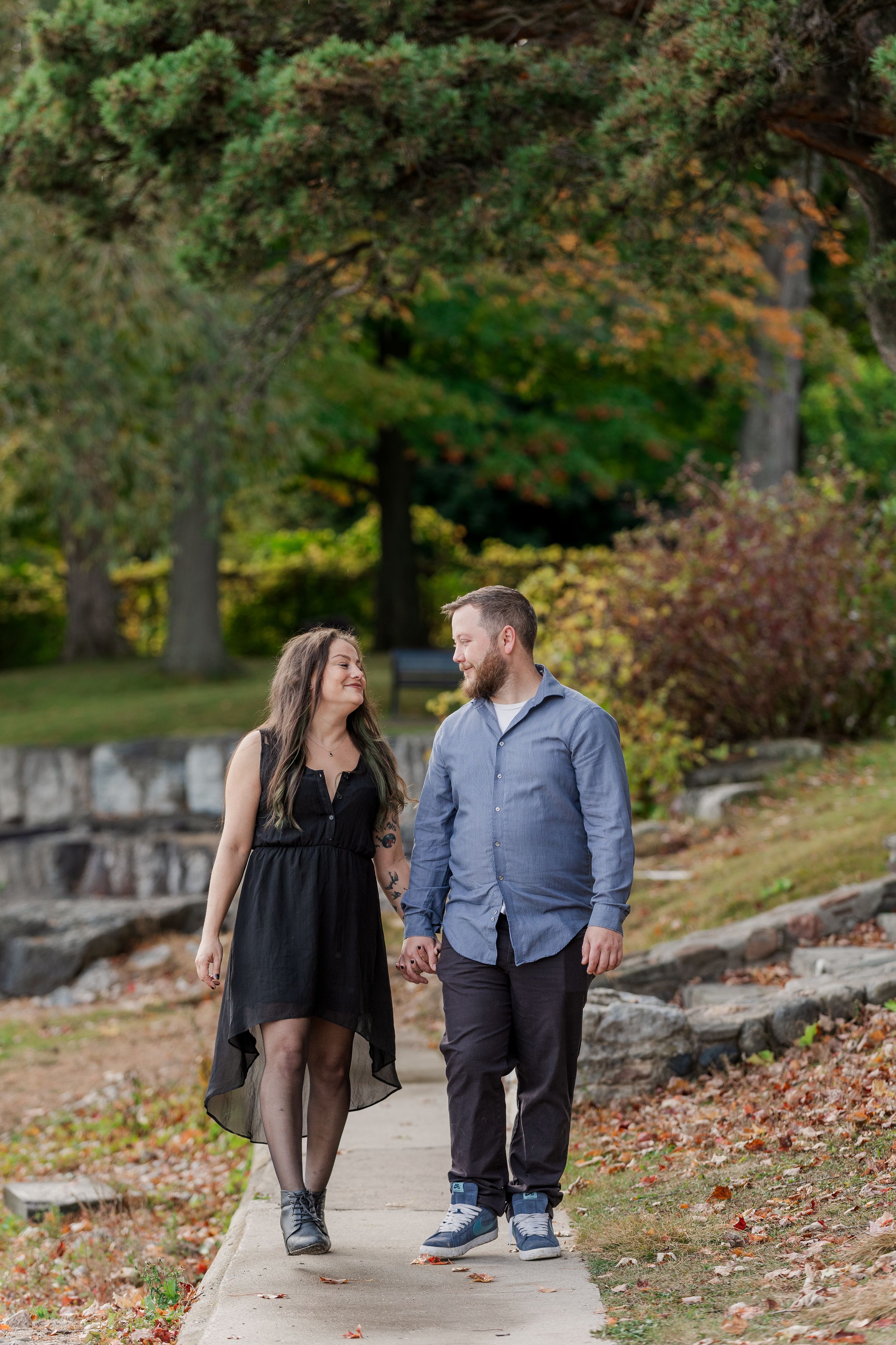 A couple walks together on a stone path surrounded by autumn foliage and trees in a romantic outdoor setting.