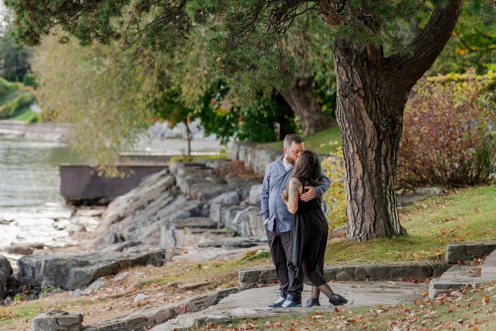 A couple enjoys a romantic autumn engagement photoshoot among fallen leaves and trees in a park setting.