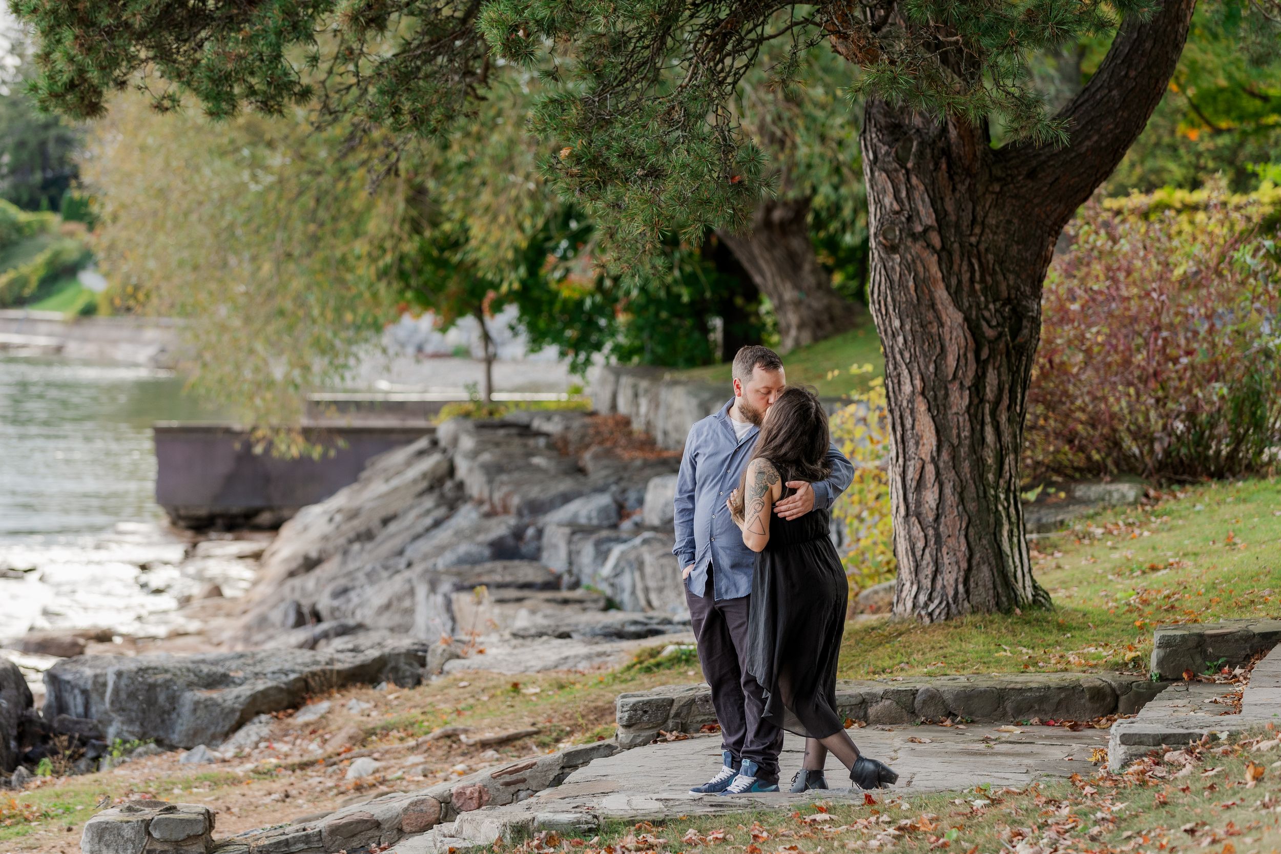 A couple enjoys a romantic autumn engagement photoshoot among fallen leaves and trees in a park setting.
