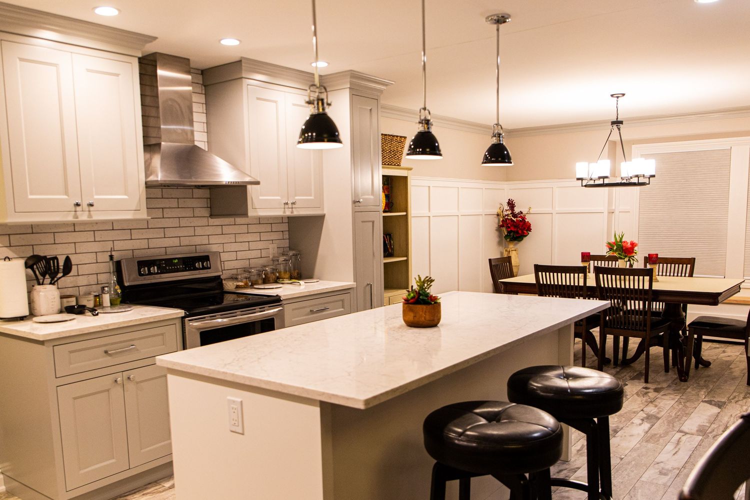 Panoramic view of a modern white kitchen with marble countertops, pendant lights, and brick accent wall.