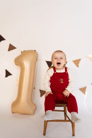 Excited baby in red outfit sits on chair with gold balloon decoration.