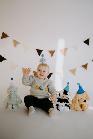 Baby celebrates with stuffed animal friends wearing party hats under festive bunting.