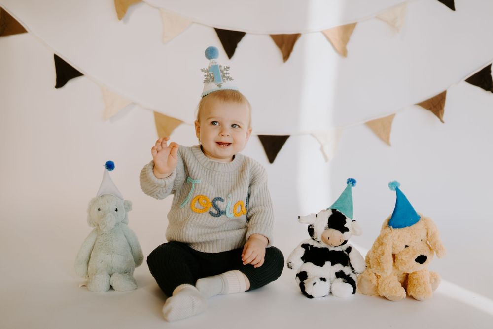 Festive birthday setup with stuffed animals and triangle banner decorations against white wall.