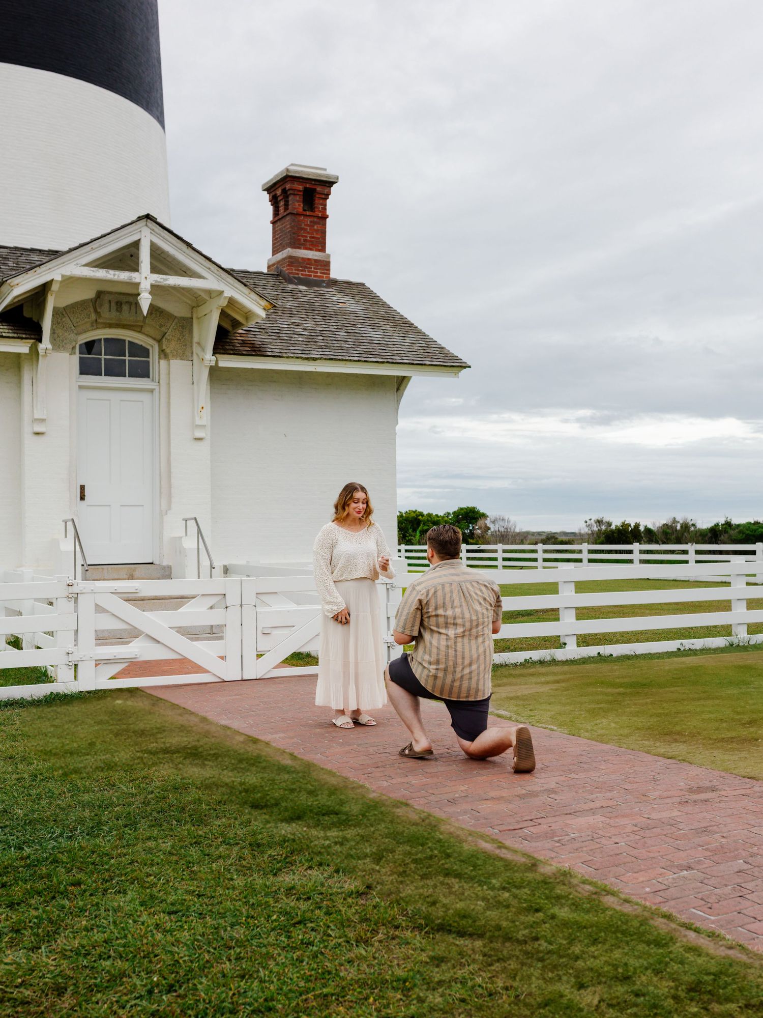 Surprise proposal moment captured at a white farmhouse with picturesque white fence.