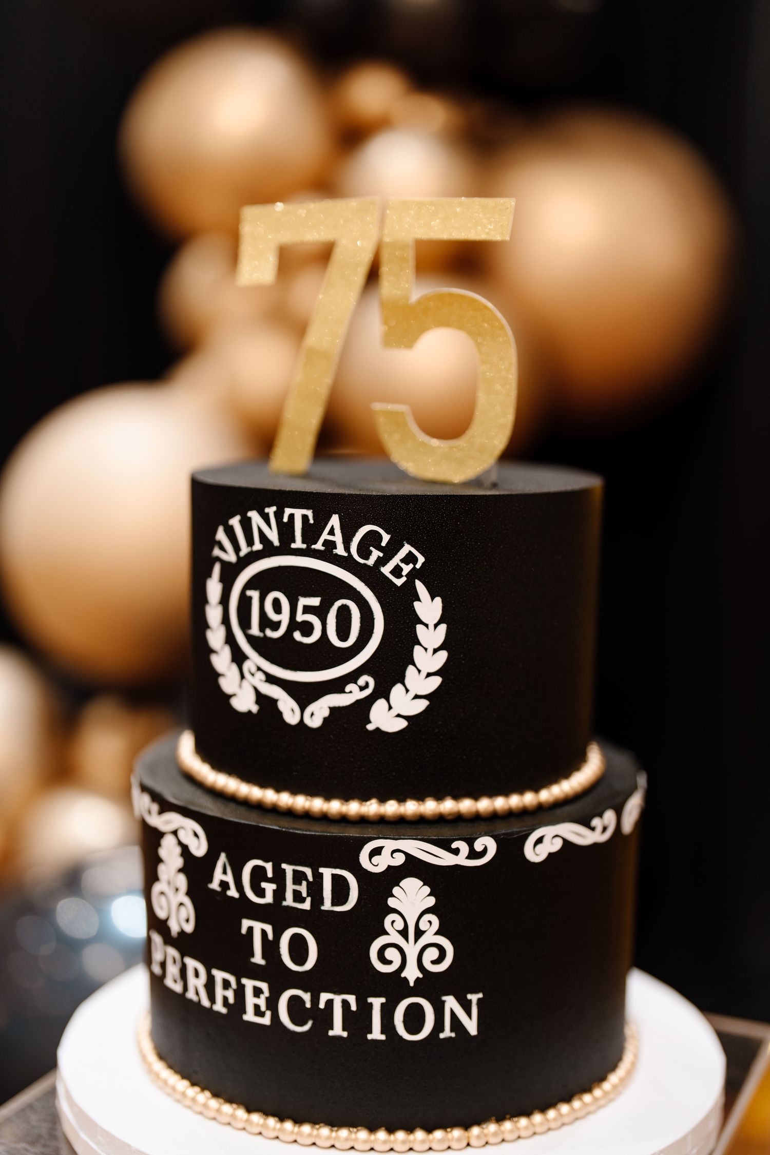 Black two-tier 75th birthday cake with gold vintage 1950 aged to perfection design.