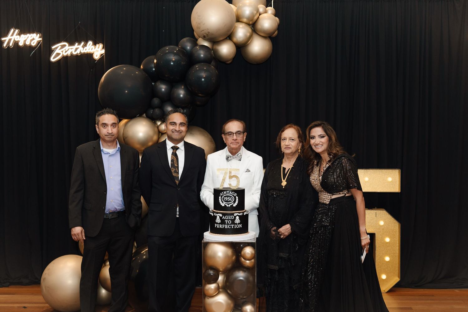 Family group photo with 75th birthday cake at black and gold party celebration.