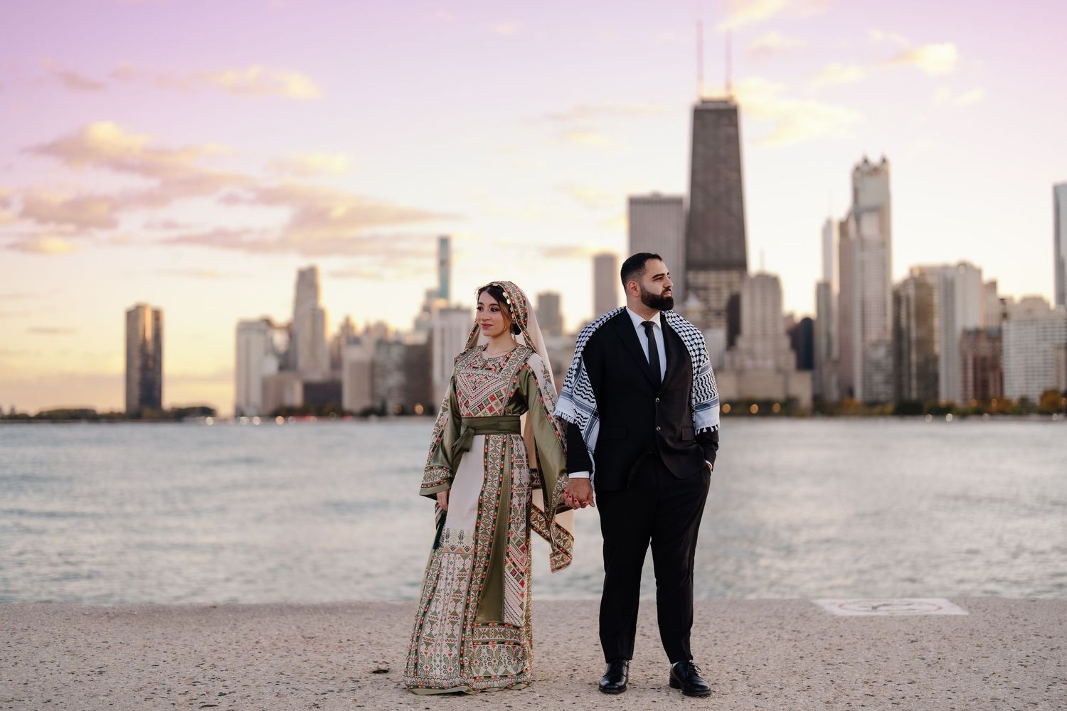 Muslim couple holding hands in traditional South Asian wedding attire with Chicago skyline at sunset.