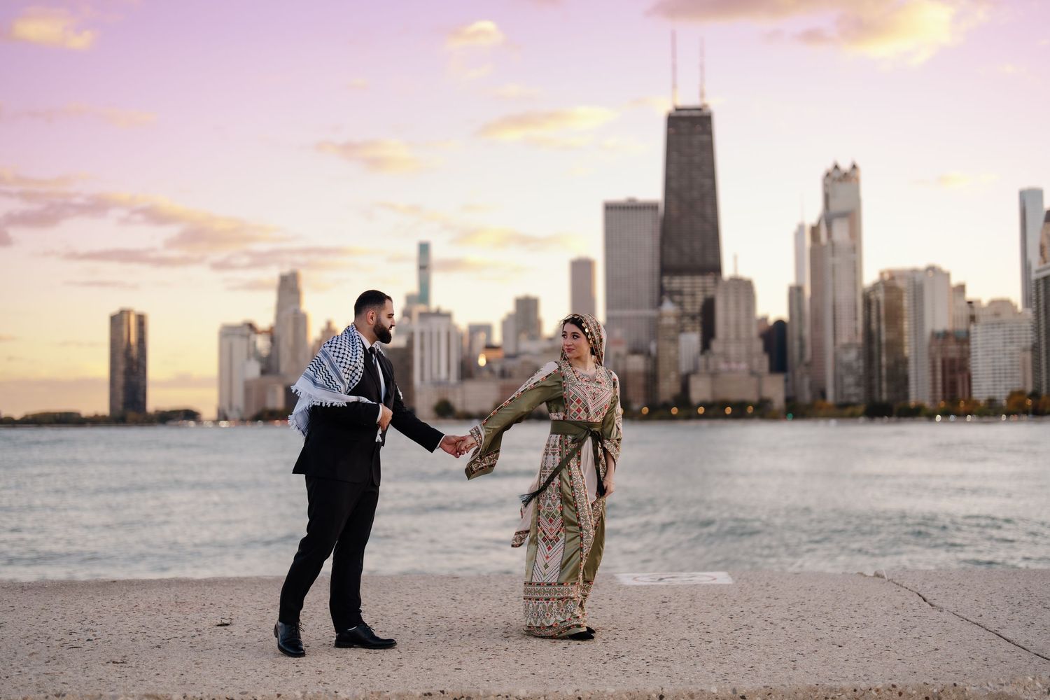 A couple holding hands on Chicago lakefront at sunset, woman in traditional embroidered sari, man in formal suit.