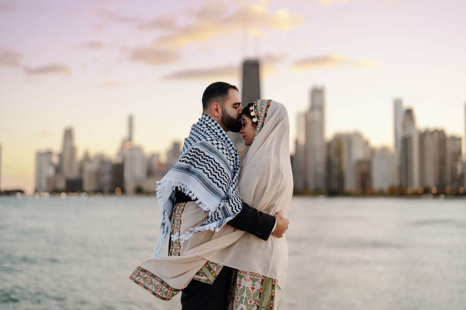 A couple sharing a kiss on Chicago lakefront at sunset, wearing traditional Palestinian keffiyeh and embroidered dress.