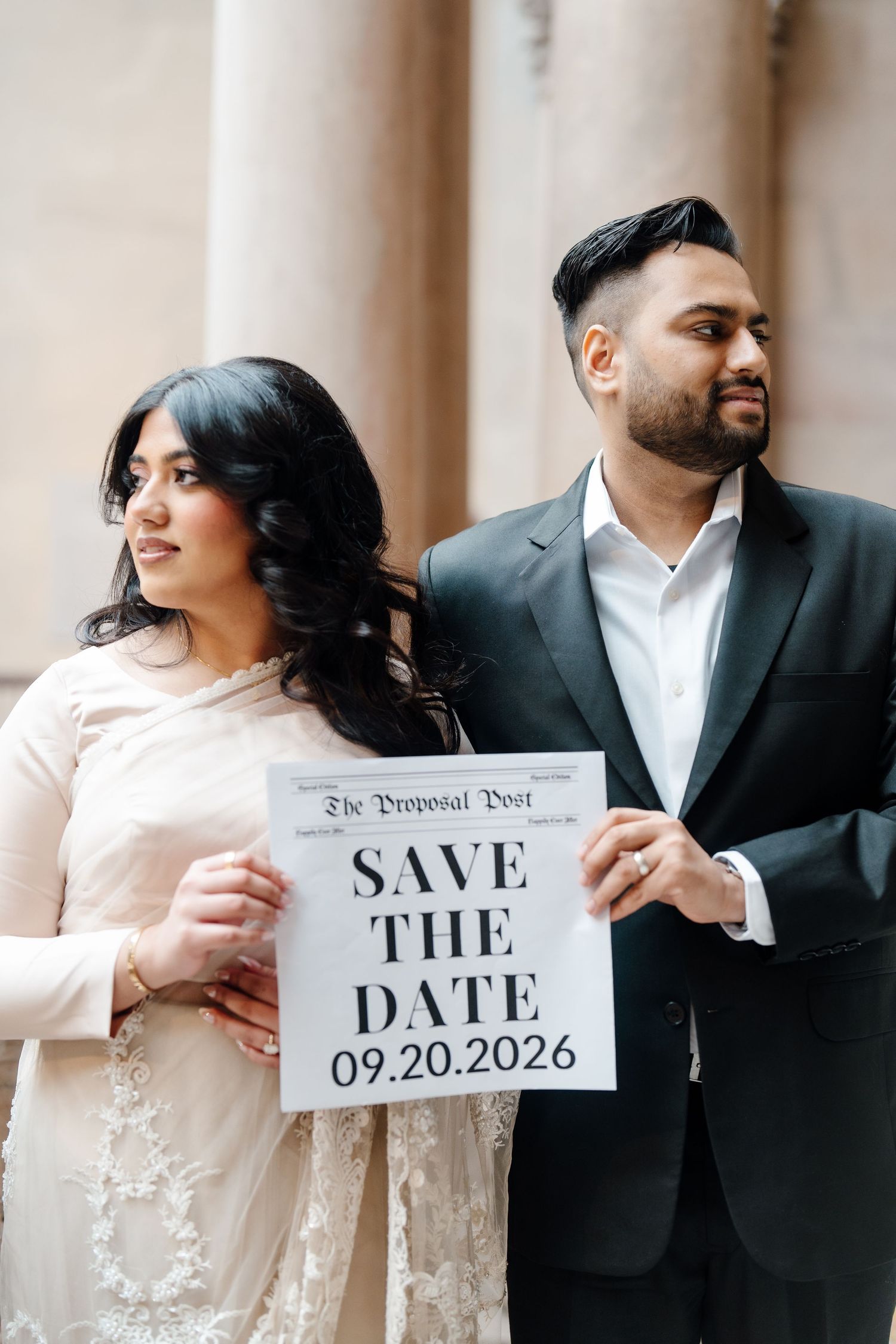 Couple holds Save the Date sign for 09.20.2026 wedding near elegant columns.