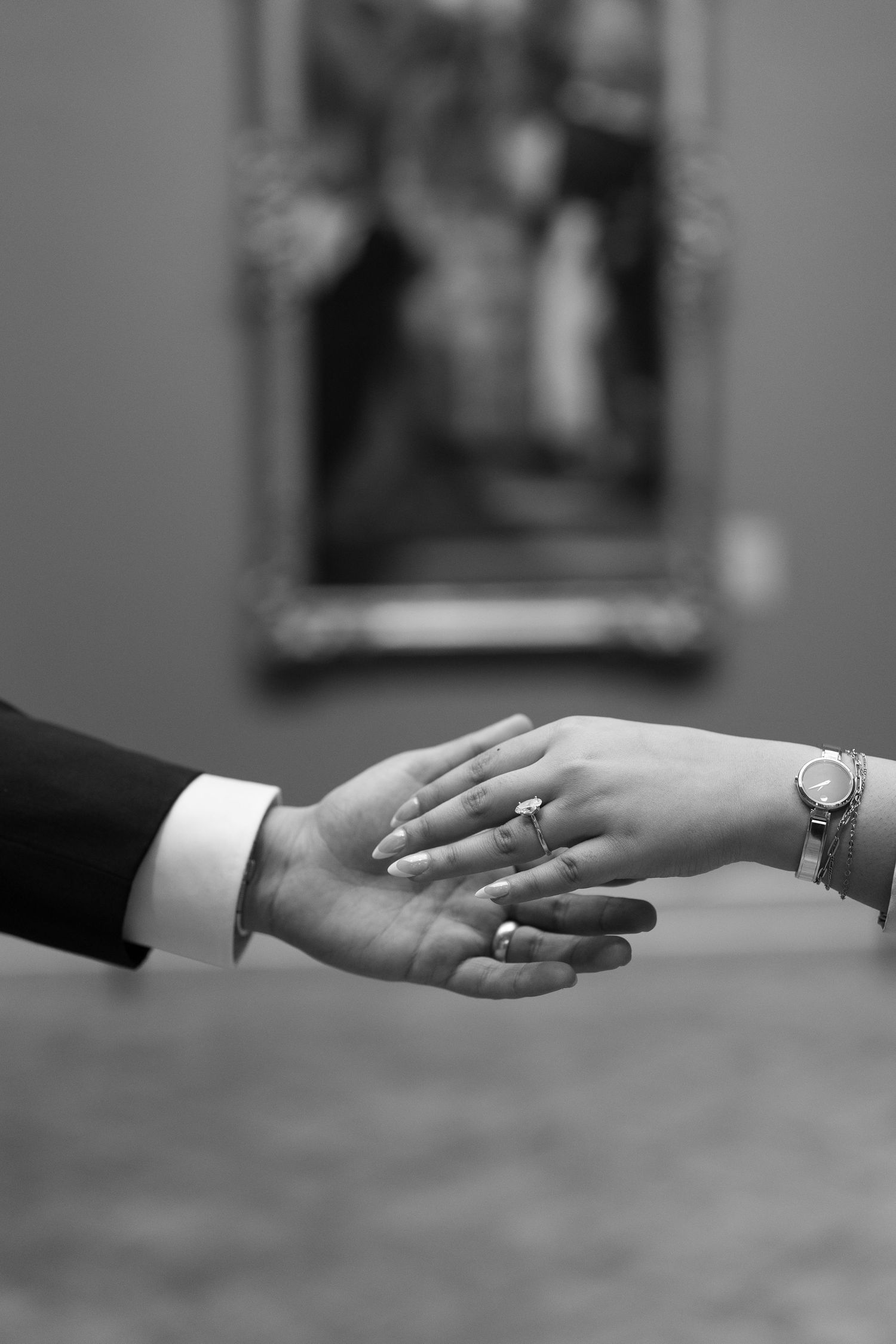 Black and white close-up of engaged couple holding hands showing diamond engagement ring.