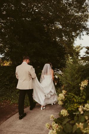 Bride and groom walk hand in hand along garden path after outdoor wedding ceremony.