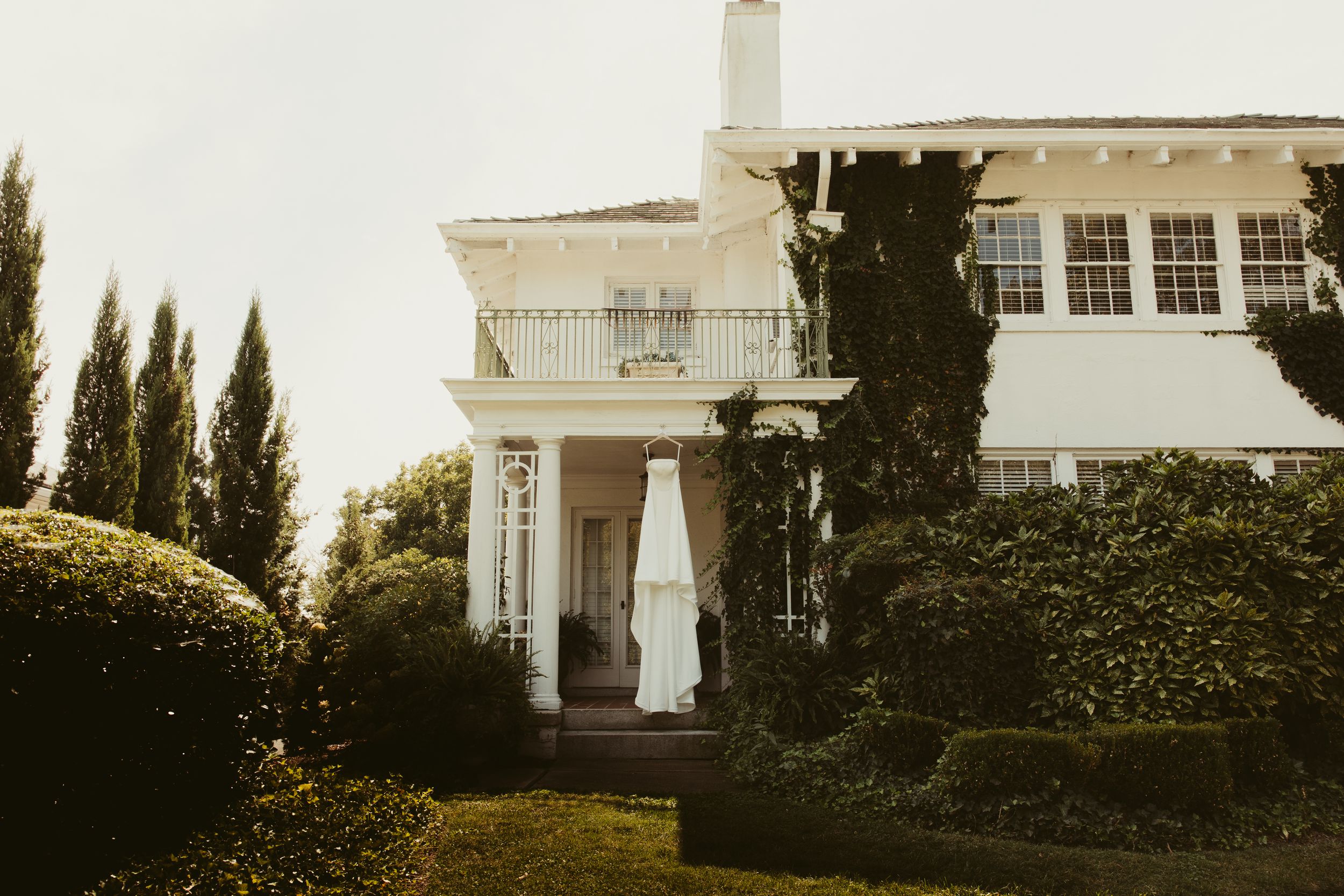 White wedding gown hangs outside an elegant ivy-covered Southern mansion venue.