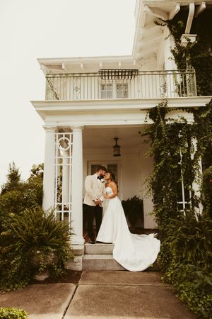 Bride and groom share a romantic moment on the steps of an ivy-covered white mansion wedding venue.