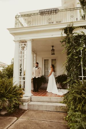 Bride and groom share first look on steps of elegant white Southern mansion.