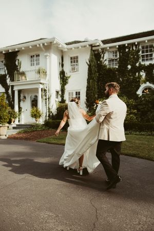Newlywed couple walks hand-in-hand toward an elegant ivy-covered white estate wedding venue.