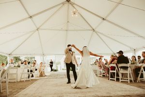 Bride and groom share first dance under white tent with string lights at reception.