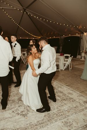 Bride and groom share an intimate dance under string lights inside a elegant tented wedding reception.