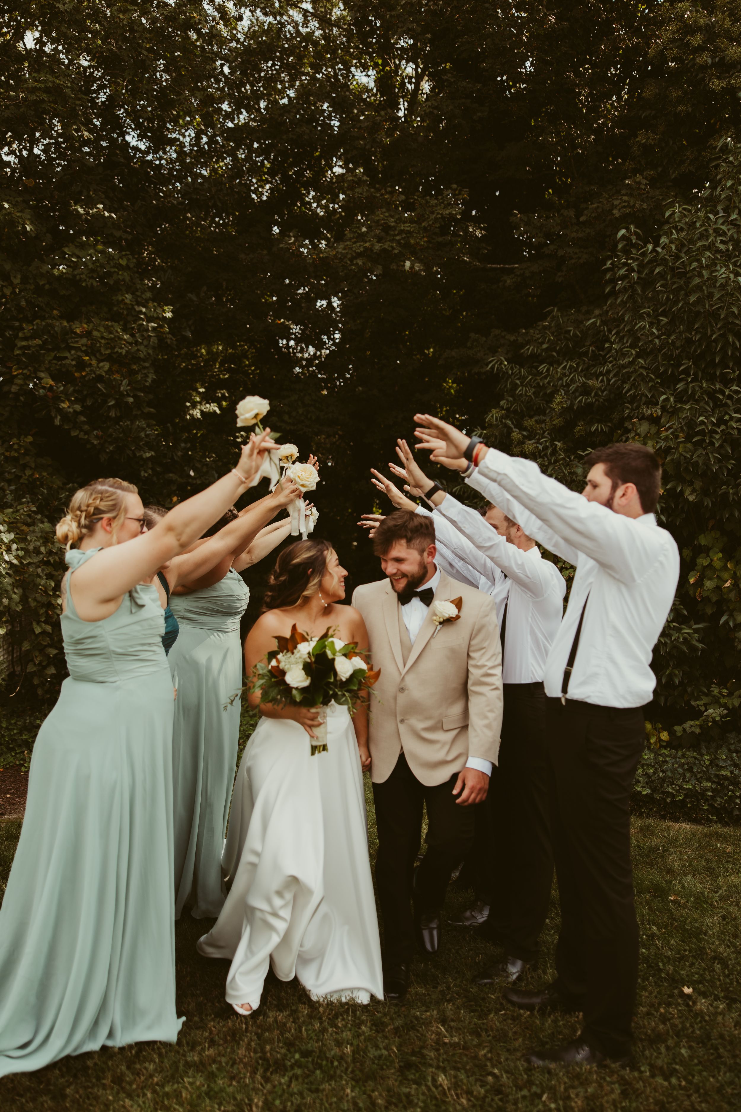 Wedding party celebrates with raised bouquets as bride and groom walk through an arch of hands at The Finch House in Thomasville, NC.