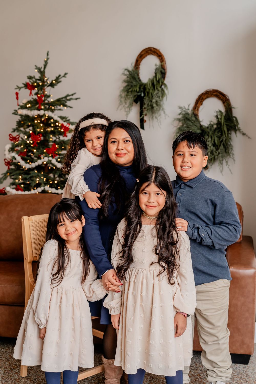 Family poses together in coordinated outfits in front of a decorated Christmas tree for holiday photos.